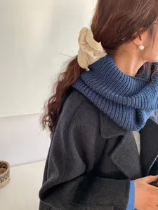 Close-up of a thick blue knitted cowl scarf worn by a model in a cozy winter setting