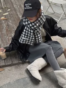 Close-up of black and white checkered knitted scarf worn by a model in street style setting.