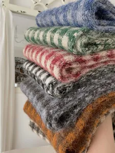 Close-up of a stack of cozy mohair-textured knit scarves in various plaid patterns