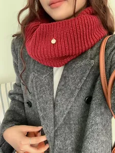 Detailed view of a thick red knitted neck warmer with a small gold metal tag.