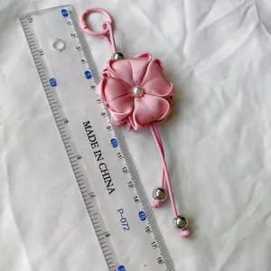 Detailed macro view of pink ribbon flower keychain charm next to a ruler for scale