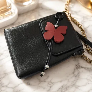 Close-up of black textured PU leather pouch with red butterfly charm and gold chain