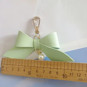 Mint green PU leather bow keychain with pearl pendant measured against a wooden ruler