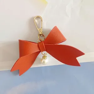 Detailed close-up of a red PU leather bow keychain with gold clasp and pearl charm.