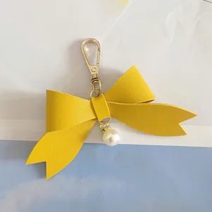 Detailed close-up view of a vibrant yellow PU leather bow keychain with a pearl charm.