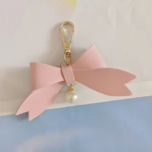 Detailed view of a pink PU leather bow keychain featuring an elegant white pearl charm