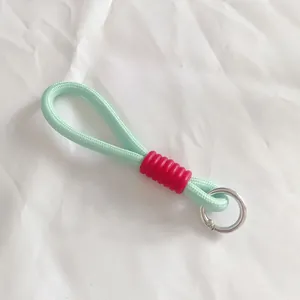 Detalle del cordón trenzado verde menta con funda roja estriada y anillo plateado