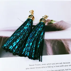 Macro shot of teal metallic leather tassel charms with gold-tone hardware on a book page.