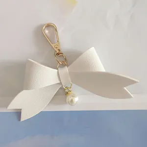 Macro detail of a white PU leather bow keychain featuring a gold clasp and pearl pendant
