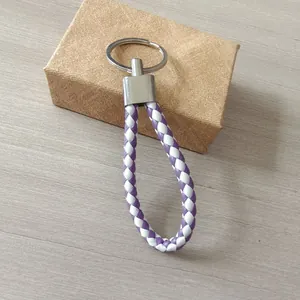Primer plano de un llavero de cuero trenzado morado y blanco sobre una caja de regalo.