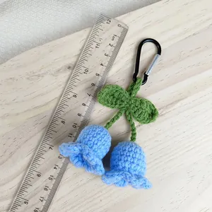 Llavero de lirio de los valles tejido a mano en azul con mosquetón negro y fondo de madera