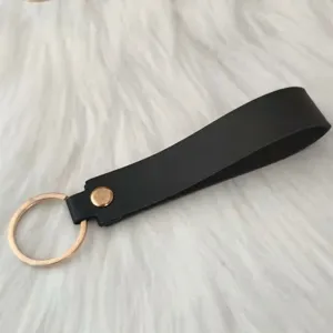 Close-up of minimalist black leather strap keychain with gold metal ring and stud fastener