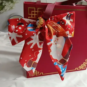 Close-up of a festive red Christmas silk scarf tied as a bow on a red gift box handle.