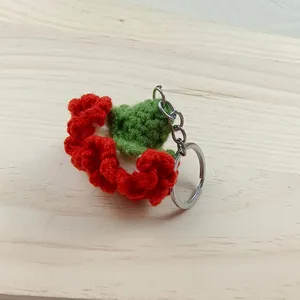 Detailopname van een handgemaakte rood-groene gehaakte anjer-sleutelhanger op hout
