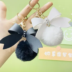 Close-up of leather bow keychain with soft white and black faux fur pom-poms.