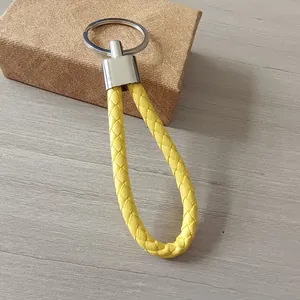 Llavero de cuero trenzado amarillo hecho a mano con anillo de metal plateado en madera