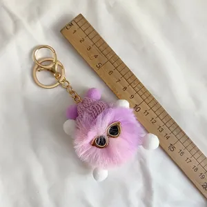 Detailed view of a purple fuzzy monster keychain with sunglasses and a wooden ruler for size