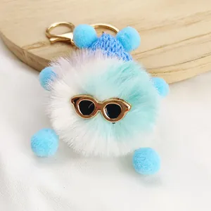 Macro view of a fluffy blue plush monster keychain with sunglasses and a gold clasp