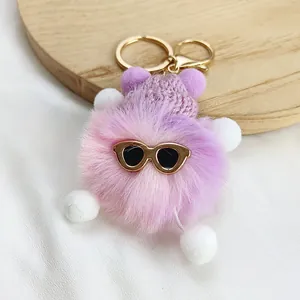 Detailed close-up of a cute purple plush monster keychain wearing stylish gold sunglasses.