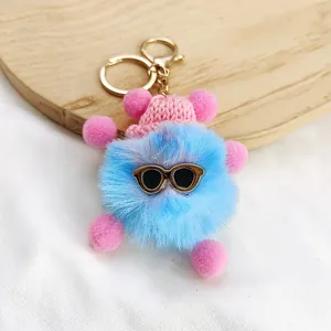 Close-up of a cute blue fluffy monster keychain with pink hat and sunglasses accessory.