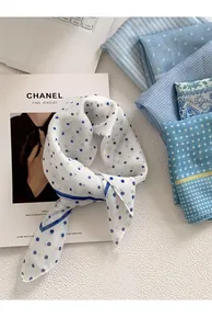 Close-up view of a white silk scarf with blue polka dots tied in a knot on a white texture