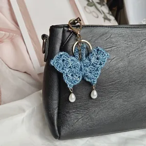 Hand-crocheted blue butterfly bag charm with white pearl drops on a black bag