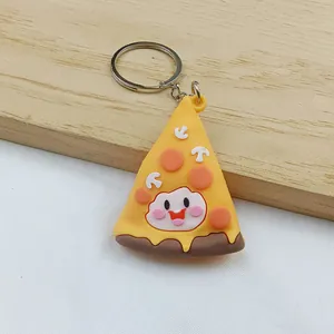 Close-up of a cute cartoon pizza slice keychain with a smiling face on a wooden surface.