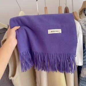 Macro view of a soft purple knit scarf featuring elegant tassels and a white label