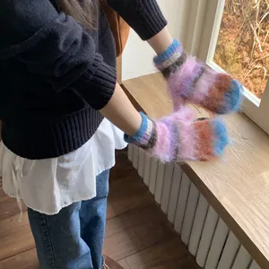 Close-up of colorful fuzzy knit mittens worn by a person in a cozy winter indoor setting