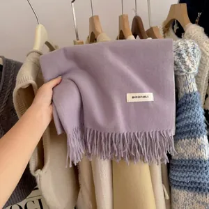 Close-up of a soft purple knitted scarf with tassels and a minimalist brand label.