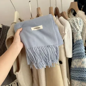 Close-up detail of a soft blue knitted scarf with fringes and a minimalist brand tag