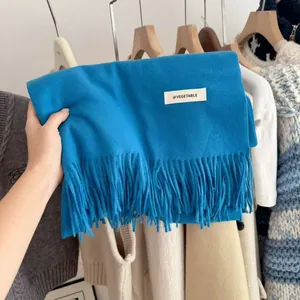 Close-up view of a vibrant blue knitted winter scarf featuring fringes and a minimal label