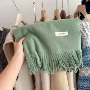 Close-up of a soft mint green knitted scarf with fringe and a minimal white label.