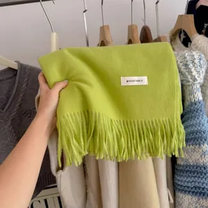 Detailed view of a bright lime green knit scarf with long tassels and a small white label