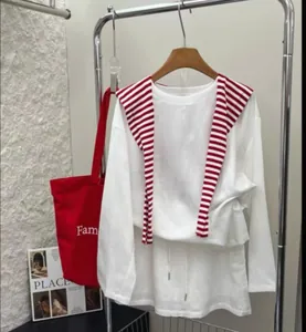 Detalle de un conjunto casual blanco con un accesorio de chal a rayas rojas y blancas.