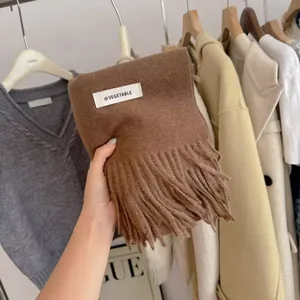 Detail view of a cozy brown knitted scarf with tassels and a minimalist brand label.