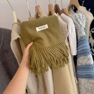 Detailed view of olive green solid color knitted scarf featuring decorative tassels and label