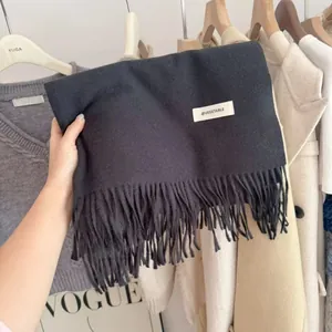 Close-up of a thick dark grey knit scarf featuring fringe details and a white brand tag.