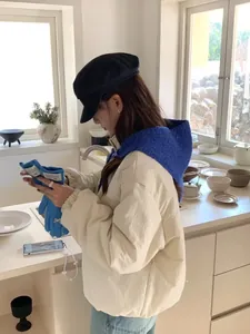 A vibrant blue knitted triangle scarf and hooded shawl worn in a warm indoor setting.