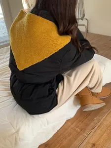 Detail showing a mustard yellow knitted triangle scarf worn over a black puffer jacket.