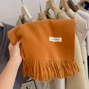 Close-up of an orange knitted scarf with fringe and a white text label detail.
