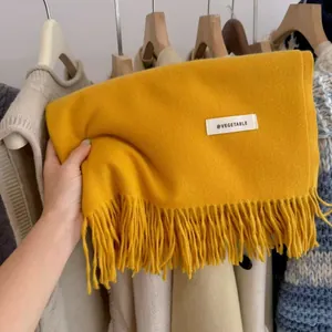 Detailed view of a thick yellow knitted scarf featuring tassels and a white fabric tag