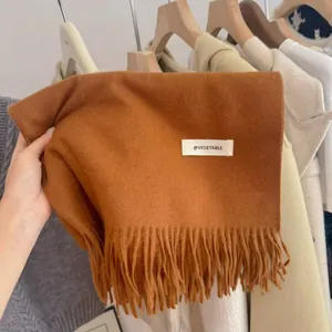 Close-up detail of a ginger knitted scarf with fringes and a white VEGETABLE woven label.