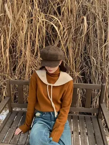 Close-up of a cream knitted detachable collar shawl worn over an orange sweater