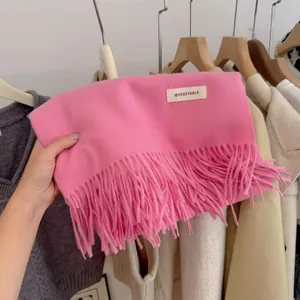 Detailed view of a soft pink knitted scarf with decorative tassels and brand label