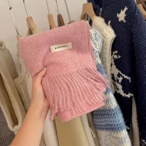 Close-up of a soft pink knitted scarf with decorative tassels and a minimalist brand label
