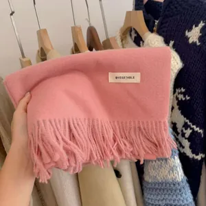 Close-up of soft pink knitted scarf with decorative tassels and brand label