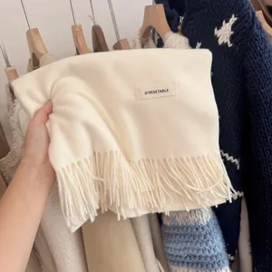 Soft cream knitted scarf close-up featuring long tassels and minimalist brand label