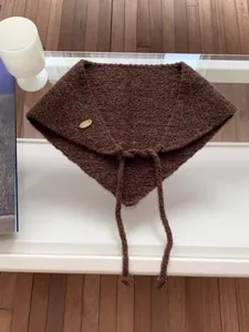 Close-up of brown knitted triangle scarf with ties and decorative wooden button detail