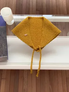 Detail of a yellow mustard knitted triangle scarf with a decorative wooden button.